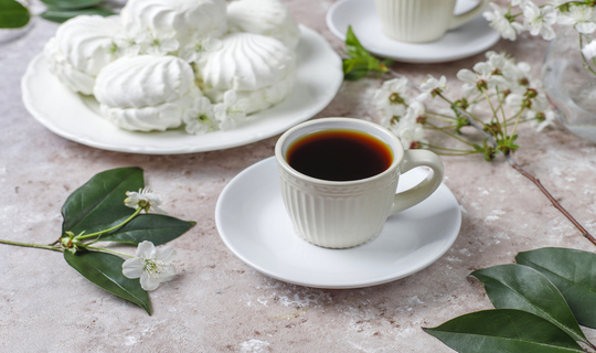 Showcasing a cup of coffee on a saucer with goodies and flowers surrounding, that complements a relaxing, transformed life..