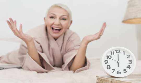 Blond haired woman smiling happily beside a clock knowing she has found the key to slowing down the aging process.