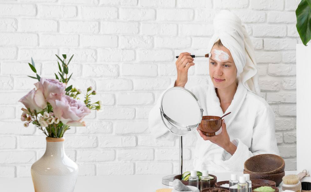 Woman in a robe and a towel on her head starting to give herself a facial.