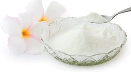 Pearl Powder in a crystal bowl with a spoon of Pearl Powder, and two white flowers with yellow centers beside it.