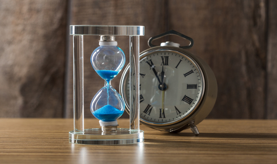 Hour glass filled with blue sand and an alarm clock signifies the passing of age.
