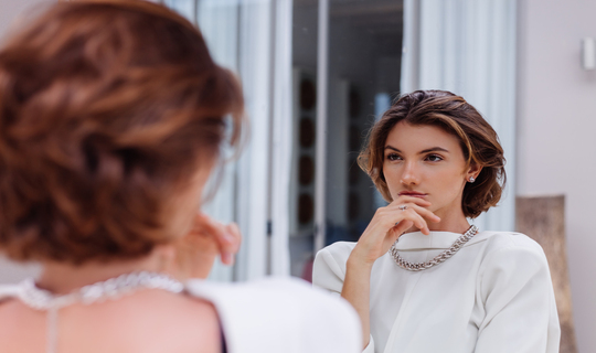 Pretty brunette lady looking at her reflection grateful that she looks younger than she actually is.