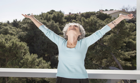 Happy carefree senior woman standing with head back, arms raised, smiling and enjoying life.